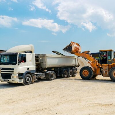 Excavator loading materials into a heavy-duty truck at a sunny construction site.