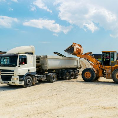 Excavator loading materials into a heavy-duty truck at a sunny construction site.